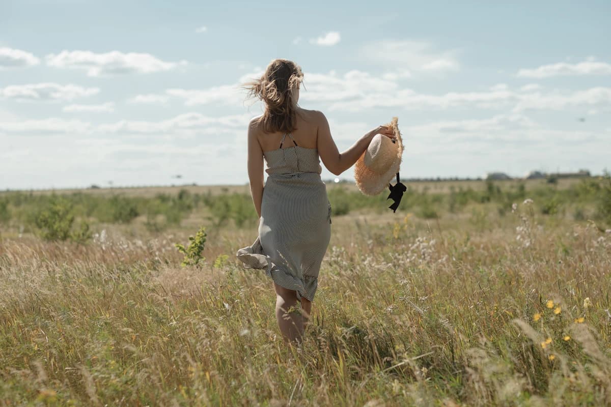 A woman walking through a summer field holding a straw hat